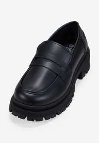 Mocassini in pelle nera con suola spessa e scanalata. Presentano una fascia larga sopra il collo del piede e una superficie liscia sulla parte superiore.