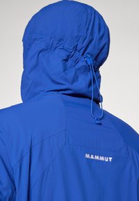Sinine välistingimustes kasutatav jakk kapuutsiga, millel on reguleeritav nöör ja seljal helendav "Mammut" logo. Sile ja kerge kangas.