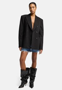 Zwart dubbelgebreid blazer met grote revers, gecombineerd met distressed denim shorts en slouchy zwarte laarzen met stippen.