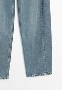 Jasnoniebieskie dżinsy z denimu o prostym kroju, z efektem wyblakłego prania i postrzępionym brzegiem. Tkanina ma gładką fakturę z widocznym szwem.