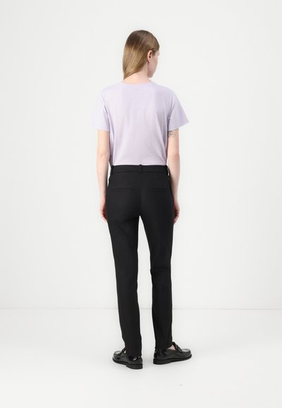 T-shirt courte à manches courtes de couleur violet clair associée à un pantalon noir sur mesure. Le pantalon est doté de poches et d'une ceinture. Le modèle est de dos.