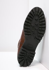 Chaussure en cuir marron avec une semelle en caoutchouc texturée. Présente des coutures décoratives et un motif de semelle pour une bonne adhérence. Taille 39 indiquée.