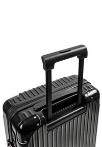 Czarna, twarda walizka z pionowymi rowkami. Posiada chowany czarny uchwyt oraz mocne akcenty w kolorze srebrnym. Zamek błyskawiczny.