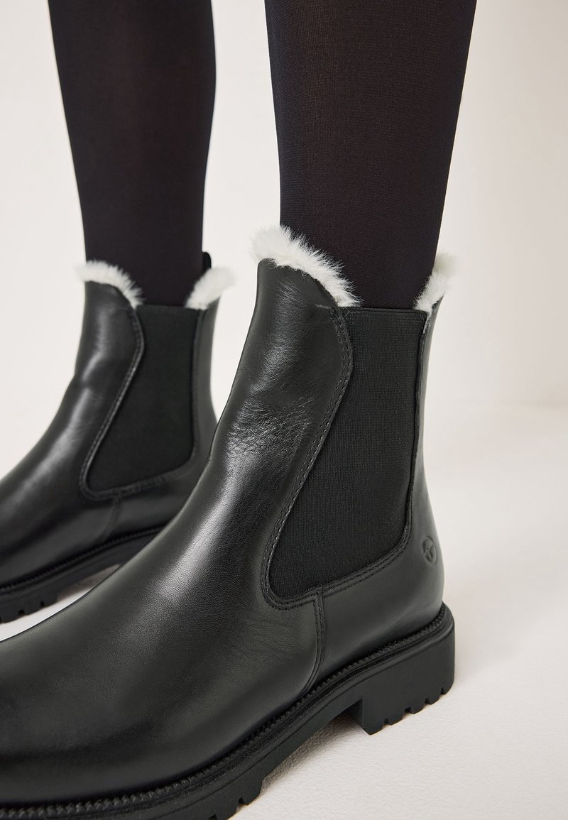 Schwarze Leder-Stiefeletten mit elastischen Seitenteilen, die einen weichen weißen Kunstfellrand am oberen Rand und eine dicke Gummisohle haben.