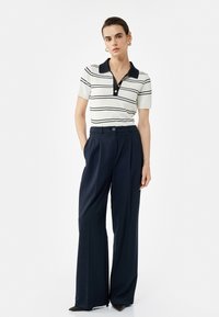 Stribet polo shirt i crème og marineblå med korte ærmer og knapdetalje, parret med højtaljede bukser med vide ben i marineblå. Struktureret stof.