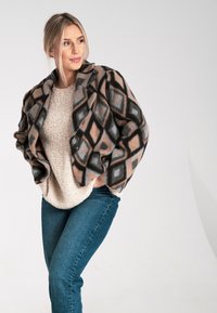 Fleecejacke mit geometrischem Muster in Brauntönen, Grau und Hellblau, mit Kragen und Knöpfen, kombiniert mit einem cremefarbenen Strickpullover und blauen Jeans.