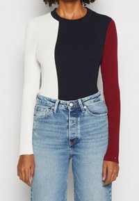 Top a maniche lunghe a righe con un design color-block in blu navy, bianco e borgogna. Abbinato a jeans in denim blu chiaro.