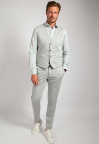 Lichtgrijze vest met bruine knopen over een lichtblauw overhemd, gecombineerd met bijpassende grijze broek en witte sneakers. Subtiele textuur zichtbaar.
