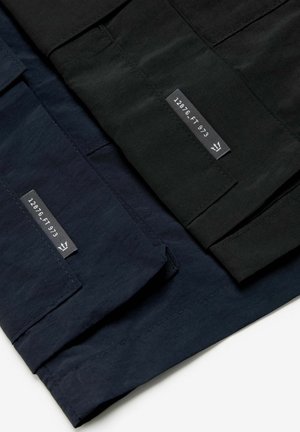 Kolm paari pükse mustas, tumesinises ja tumesinises kangas, millel on siltidega tekst. Materjal on sile ja mati viimistlusega.