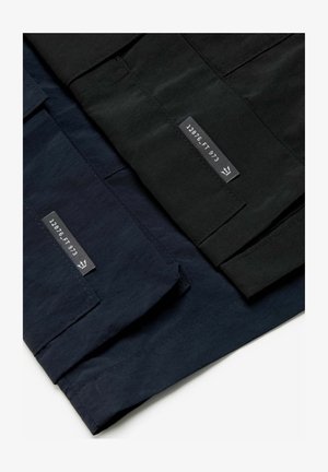 Kolm paari pükse mustas, tumesinises ja tumesinises kangas, millel on siltidega tekst. Materjal on sile ja mati viimistlusega.