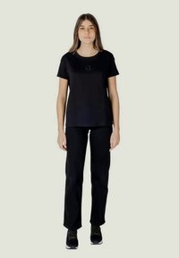 Must have lühikeste varrukatega must T-särk ümmarguse kaelusega ja peene esidetailiga, koos mustade sirgete pükste ja mustade jooksujalatsitega.