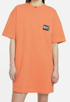 Orange oversized t-shirt featuring a round neckline, short sleeves, and a front pocket with a black Nike logo patch. Soft texture.