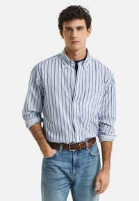 Gestreiftes Langarmhemd aus blauem und weißem Baumwollstoff mit Button-Down-Kragen und Brusttasche, kombiniert mit blauen Jeans und einem braunen Gürtel.