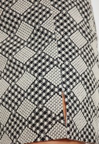 Tissu cu un model alb-negru care prezintă un design geometric cu pătrate și un detaliu cu slit. Materialul are o țesătură texturată.