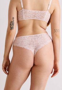 Bralette en dentelle et string assorti en rose clair. Présente des motifs floraux, des bords festonnés et des bretelles réglables. Texture lisse.