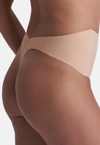 Bezszwowy bikini o wysokim stanie w miękkim beżowym kolorze, charakteryzujące się minimalistycznym designem, gładką, matową fakturą i brakiem widocznych szwów.