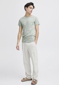 Lys grøn bomulls t-skjorte med rund hals, kombinert med løstsittende beige linbukser og brune flate sandaler, enkelt design, myk tekstur.