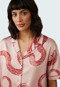 Pink silk shirt featuring a red snake pattern, short sleeves, and a notched collar with button closure. Smooth texture and semi-loose fit.