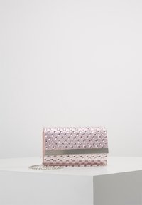 Pochette tissée en métal rose avec chaîne argentée et barre horizontale argentée sur une surface blanche contre un fond uni.
