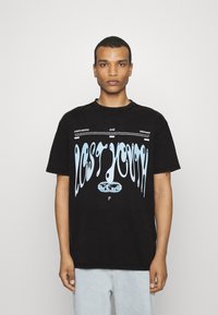 Camiseta de algodón negra con corte oversize que presenta el texto azul derretido "JUVENTUD PERDIDA" y un gráfico de un globo en el centro. Fondo liso.