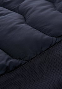Marinblå isolerad tyg med kviltade sektioner och en texturerad meshpanel. Slät och vadderad utseende med en mjuk finish.