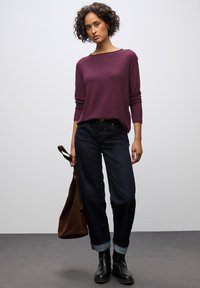 Donkerblauwe rechte jeans gecombineerd met een burgundy longsleeve top. De outfit heeft een relaxte pasvorm en opgerolde mouwen, aangevuld met zwarte enkellaarzen.