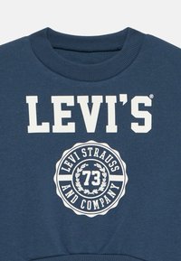 Sweatshirt bleu marine avec le logo blanc "LEVI'S" et un emblème circulaire comportant "LEVI STRAUSS AND COMPANY" et "73". Col côtelé et tissu texturé.
