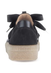 Zwarte suède sneakers met een getextureerde rubberen zool, voorzien van een zwart leren hielaccent en brede stoffen veters die aan de achterkant zijn vastgebonden.