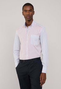 Camicia a righe con strisce verticali rosse e blu, design con colletto e taschino sul petto. Indossata con pantaloni scuri.