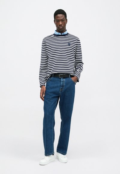 Striped long-sleeve shirt in navy and white, paired with classic blue jeans and white sneakers. Features blue collared shirt beneath.