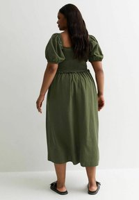 Vestido midi verde oliva con mangas abullonadas y cuerpo fruncido. Tejido suave, corte relajado y una falda fluida que llega a media pantorrilla.