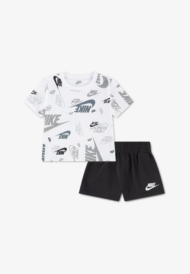 Chemise blanche à manches courtes avec des logos Nike noirs et gris partout, associée à un short noir avec un logo Nike blanc sur la jambe gauche.
