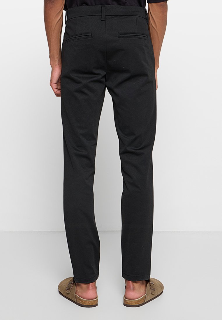 Schwarze, slim-fit Hose mit glatter Textur und zwei Gesäßtaschen. Ausgestattet mit einem Standardbund und schmal zulaufendem Bein.