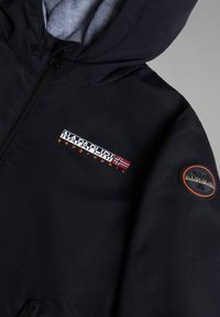 Black hooded jacket featuring a zippered front, gray inner lining, embroidered logo with Norwegian flag, and a circular patch on the sleeve.