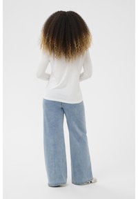 Langärmliges weißes Oberteil mit abgerundetem Saum, kombiniert mit weit geschnittenen, hellblauen Jeans aus weichem Denim und lässiger Passform.