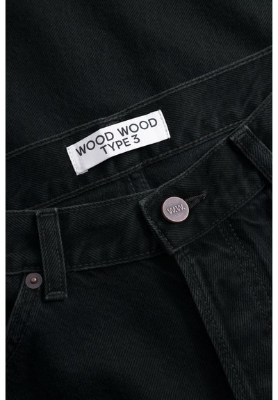 Zwarte denim broek met een wit label gemarkeerd "WOOD WOOD TYPE 3," koperen knopen en een textuurstof met een klassieke snit.