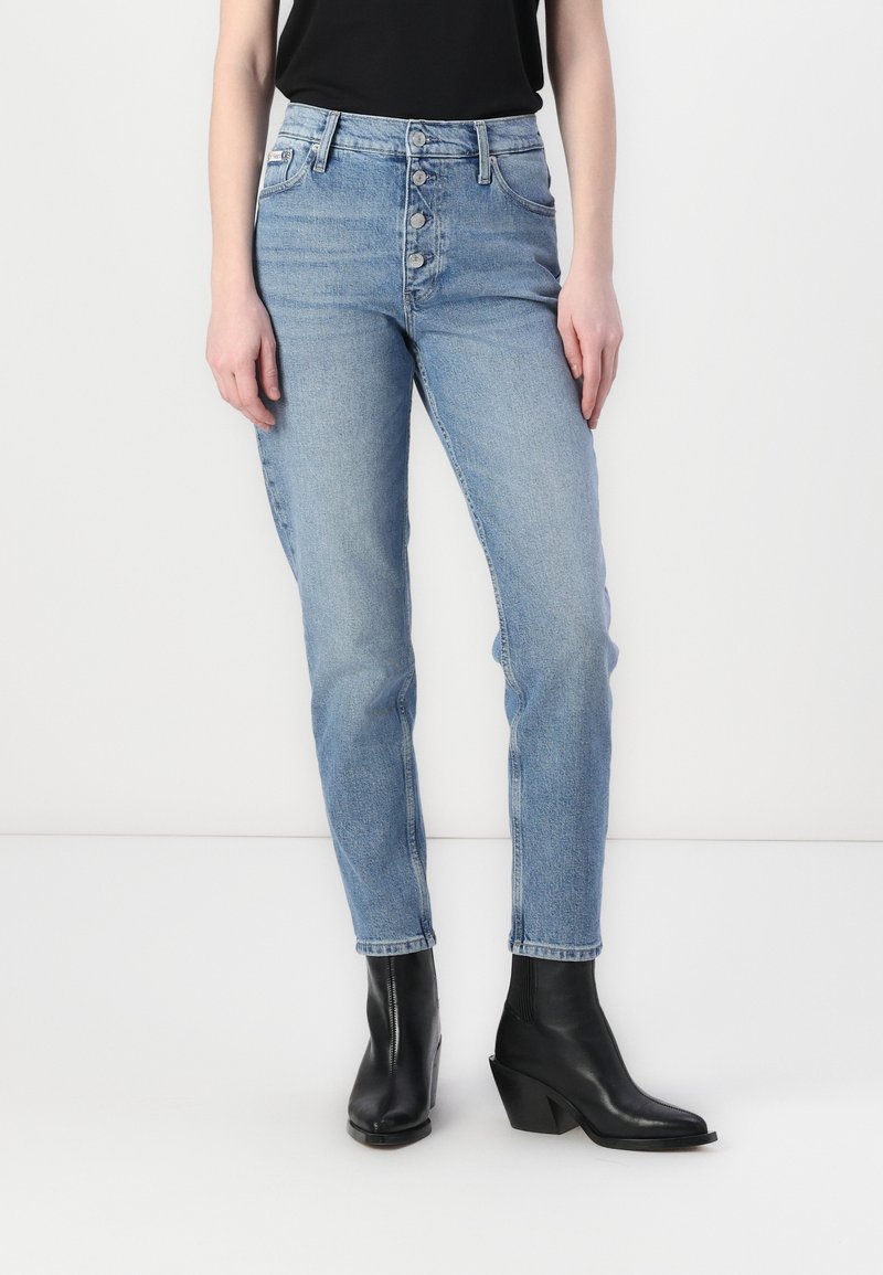 Jean taille haute bleu clair avec une coupe droite, présentant une fermeture à cinq boutons à l'avant, un design classique à cinq poches et un léger délavage.