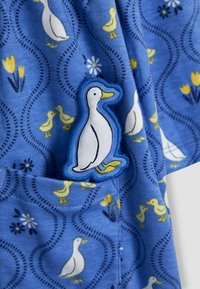 Tessuto blu con stampa di anatre con anatroccoli gialli e fiori. Un'applicazione di anatra ricamata è ben visibile sul capo.