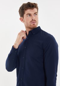 Donkerblauwe overhemd met knopen, gemaakt van een gladde stof met een kraag en lange mouwen, voorzien van een subtiele geborduurde logo op de borst.