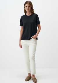 Maglietta nera a maniche corte con collo rotondo, abbinata a pantaloni bianchi slim-fit e mocassini marroni, posizionata su uno sfondo neutro.