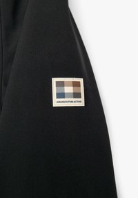 Giacca sportiva in tessuto nero con un'etichetta rettangolare di colore crema caratterizzata da un motivo a quadri multicolore e la scritta "AQUASCUTUM ACTIVE".