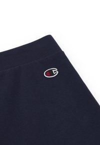 Granatowa bawełniana tkanina na bluzę o miękkiej teksturze, z małym haftowanym logo w kolorze czerwonym i białym, umieszczonym blisko górnej krawędzi.