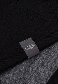 Sort stof med en glat tekstur, lagdelt over et gråt stof. Et lille gråt label med et logo er synligt på det sorte lag.