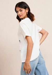 T-shirt en coton blanc à manches courtes, coupe décontractée et ourlet arrondi. Présente des accents brodés verts à l'arrière.