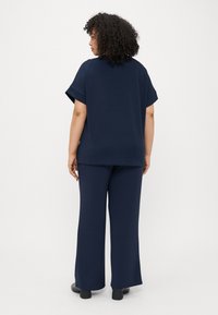 Σαλοπέτα ναυτικού μπλε σετ που περιλαμβάνει ένα χαλαρό, κοντομάνικο τοπ και παντελόνι με φαρδύ πόδι, φτιαγμένα από απαλό ύφασμα. Η πίσω όψη δείχνει απλό σχέδιο και άνεση.