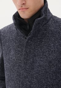 Cappotto tessuto blu navy con un colletto alto, dotato di uno strato interno con zip e un sottile motivo a macchie.