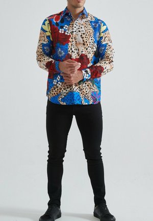 Chemise à manches longues colorée présentant un mélange d'imprimés animaliers et de motifs floraux, principalement dans des tons de bleu, rouge et crème, avec une fermeture à boutons.