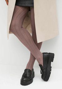 Rosa-mönstrade strumpbyxor i en mjuk mauve-färg, kombinerade med kraftiga svarta loafers med en fransdetalj och texturerad sula.
