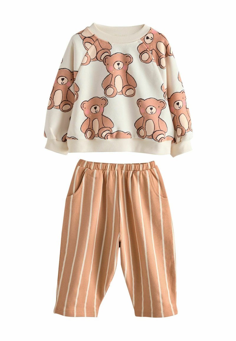 Lapsen kaksiosainen asu, jossa on kermansävyinen neuletakki, jossa on karhunprinttejä, ja vaaleanruskeat housut, joissa on valkoiset pystyradat ja etutaskut.