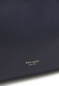 Navy leather bag with pebbled texture. Features gold "kate spade NEW YORK" logo, offering a sleek and refined design.